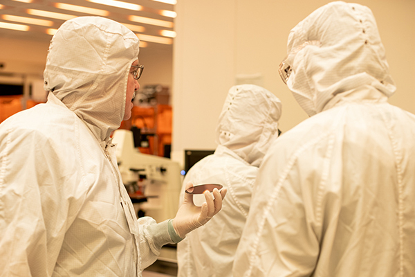 Three individuals in clean room suits inspect a silicon wafer